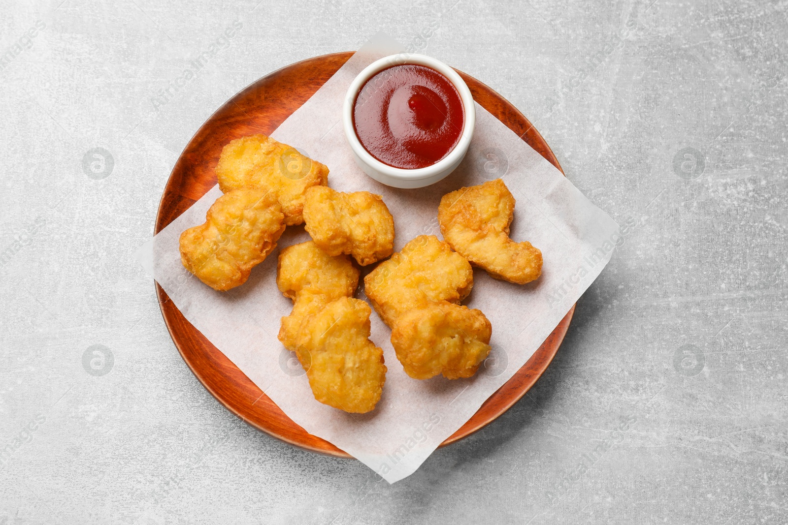 Photo of Delicious chicken nuggets and ketchup on gray textured table, top view