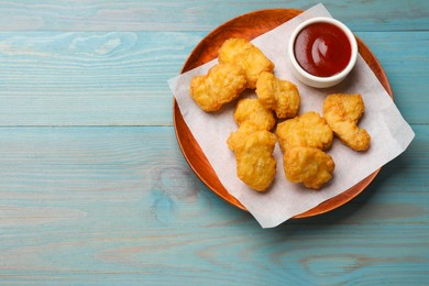 Photo of Delicious chicken nuggets and ketchup on light blue wooden table, top view. Space for text