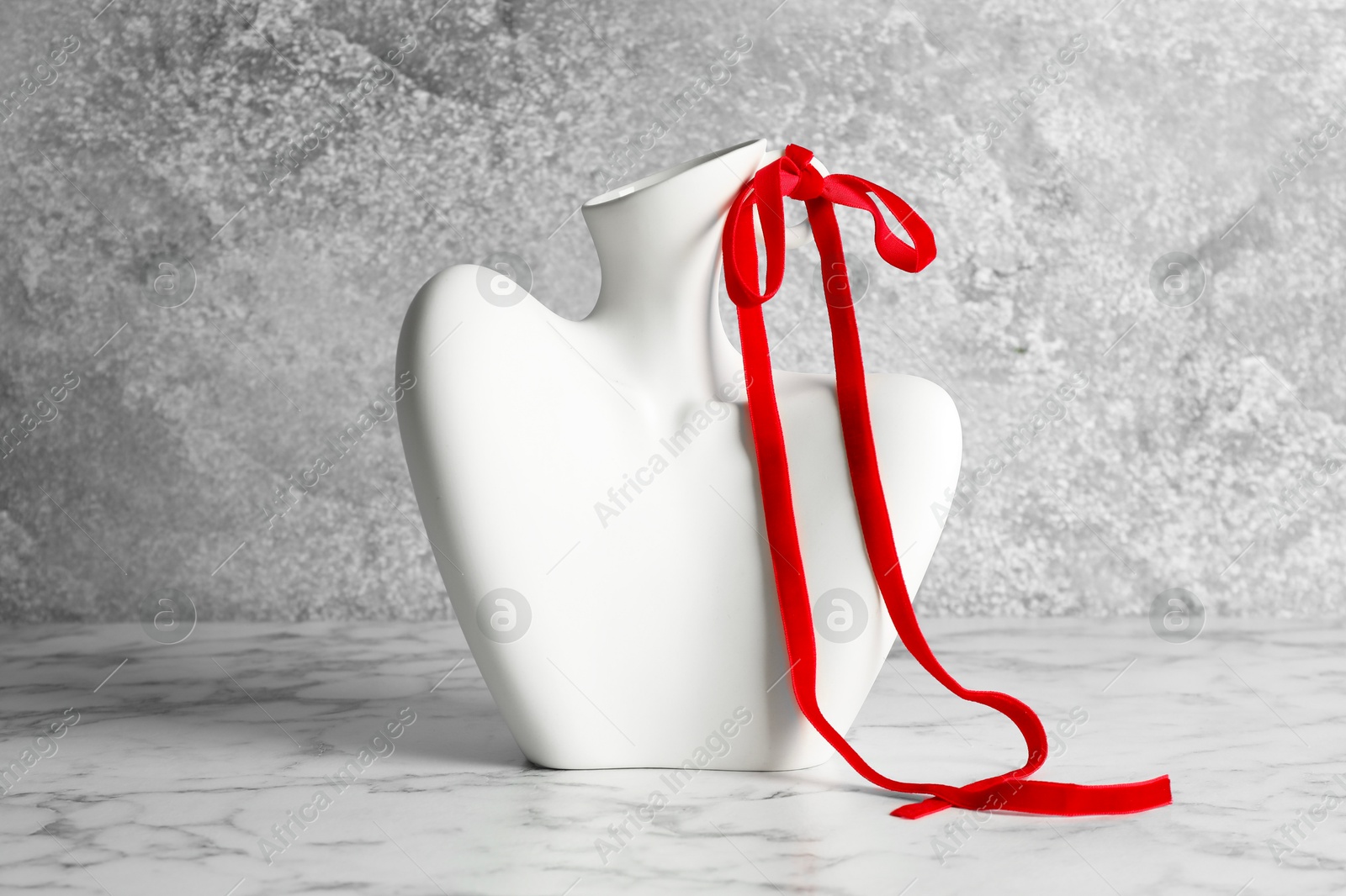 Photo of Stylish vase in shape of woman's neck with red ribbon on marble table