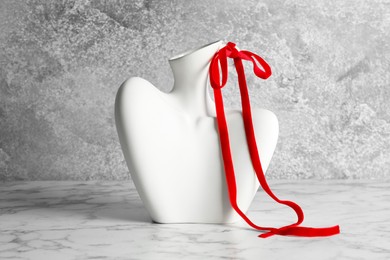 Photo of Stylish vase in shape of woman's neck with red ribbon on marble table