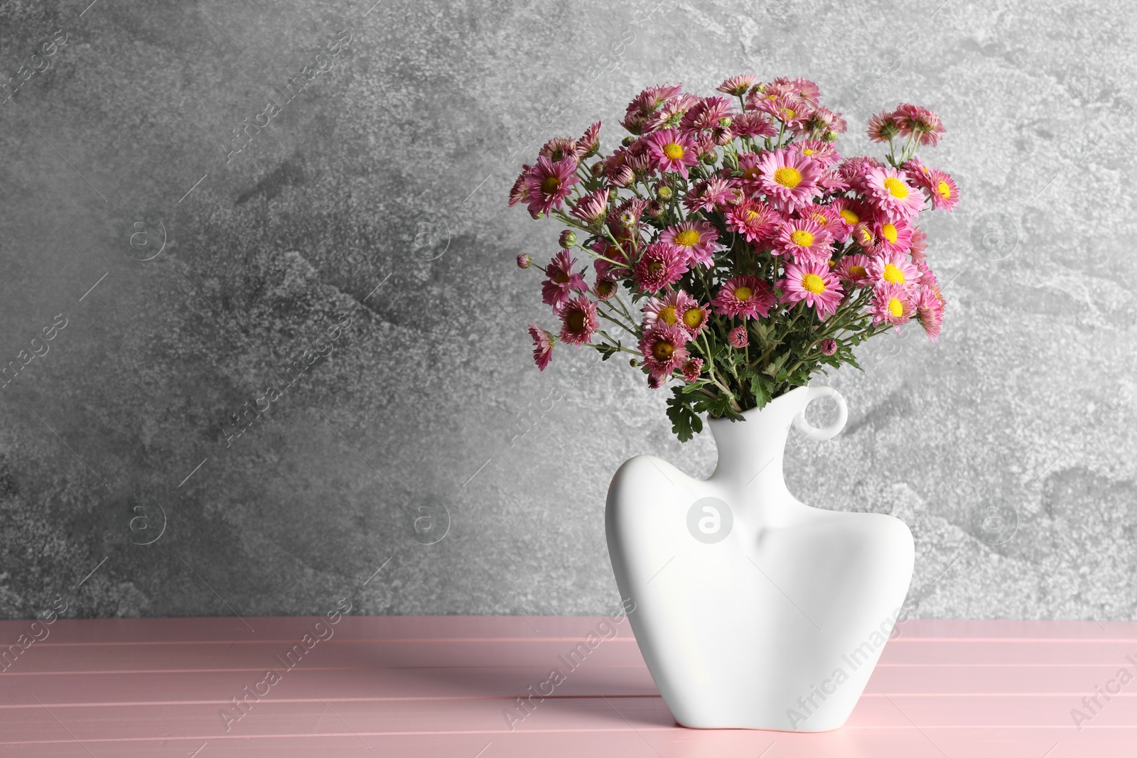 Photo of Stylish vase with beautiful flowers on pink wooden table. Space for text