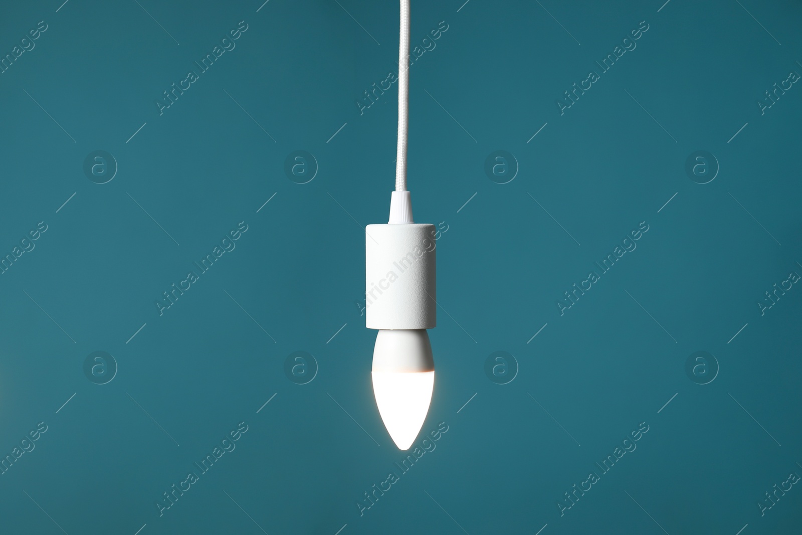 Photo of Light bulb hanging on cord against teal background