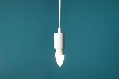 Photo of Light bulb hanging on cord against teal background