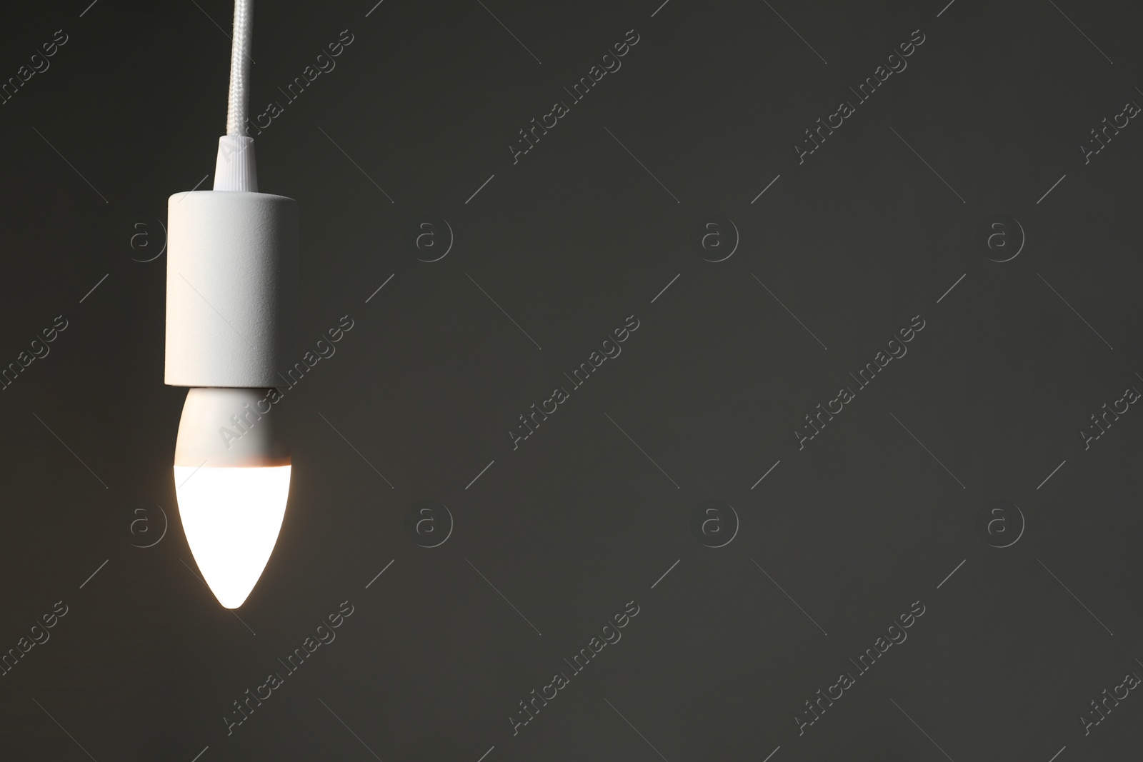 Photo of Light bulb hanging on cord against grey background, space for text