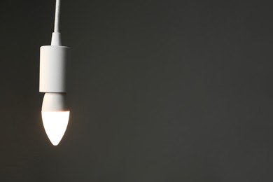 Photo of Light bulb hanging on cord against grey background, space for text