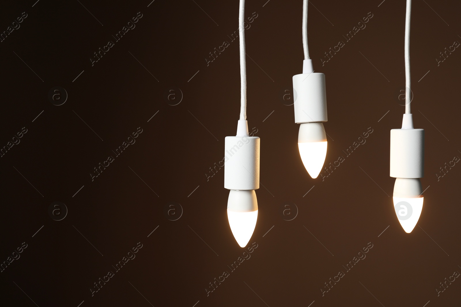 Photo of Light bulbs hanging on cords against brown background, space for text