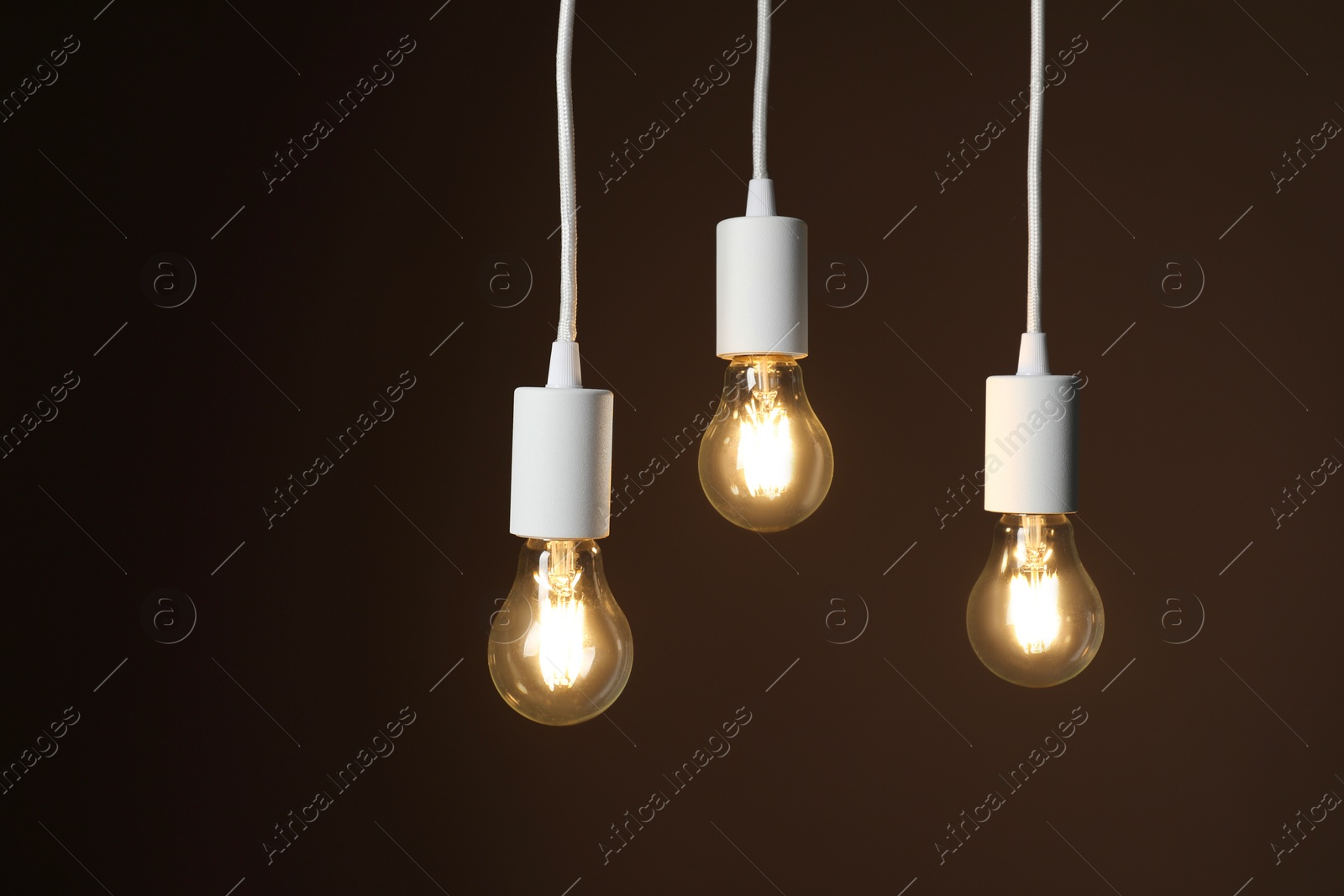 Photo of Light bulbs hanging on cords against brown background