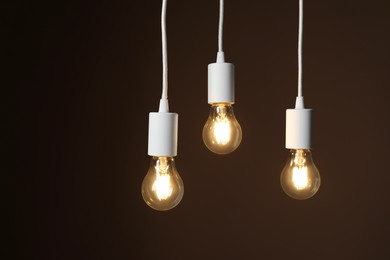 Photo of Light bulbs hanging on cords against brown background