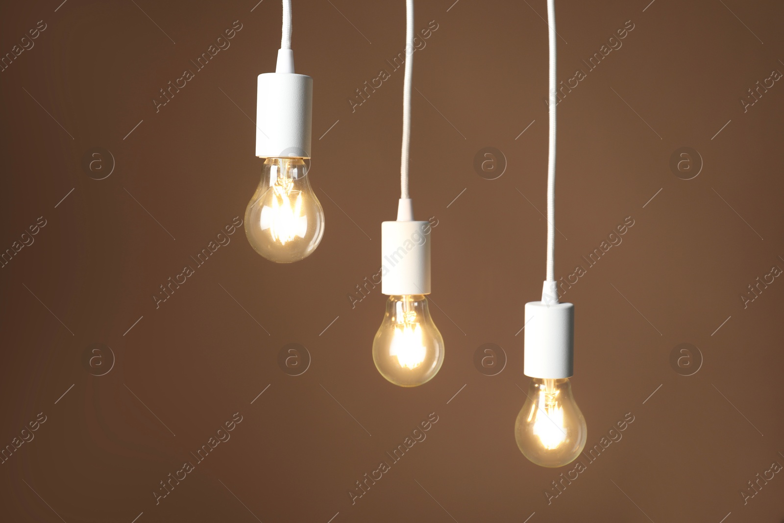 Photo of Light bulbs hanging on cords against brown background