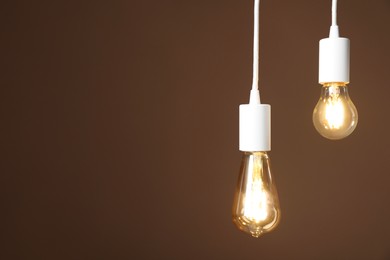 Photo of Light bulbs hanging on cords against brown background, space for text