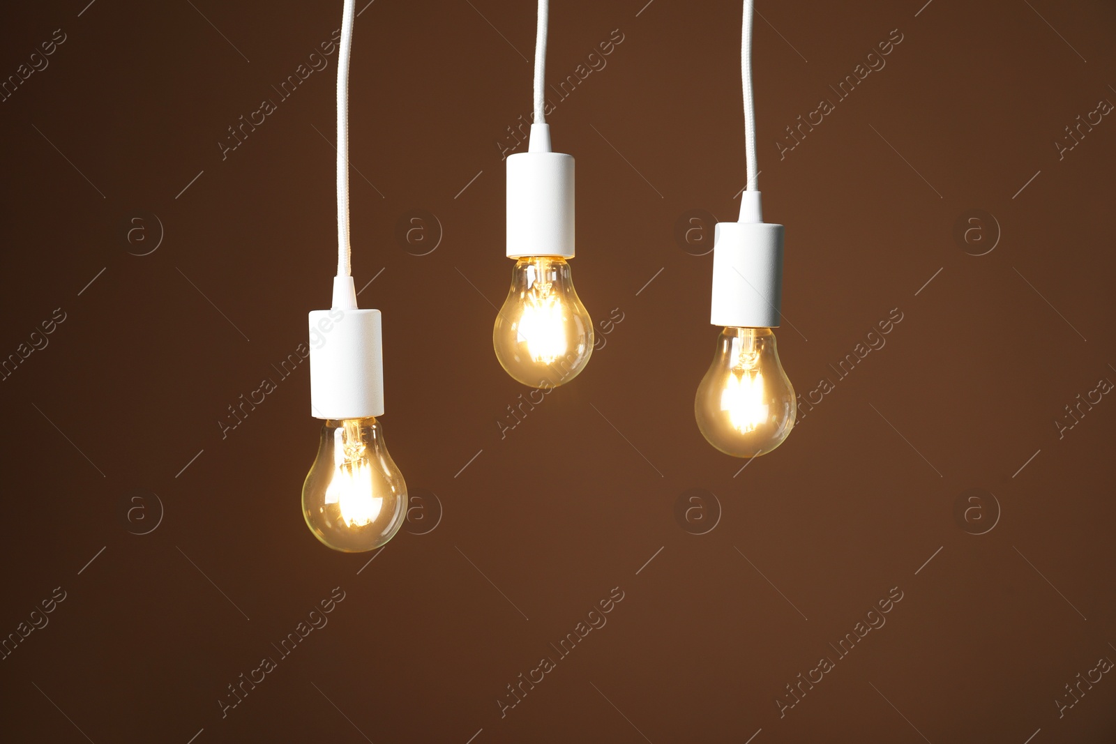 Photo of Light bulbs hanging on cords against brown background