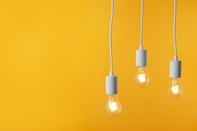 Photo of Light bulbs hanging on cords against orange background, space for text