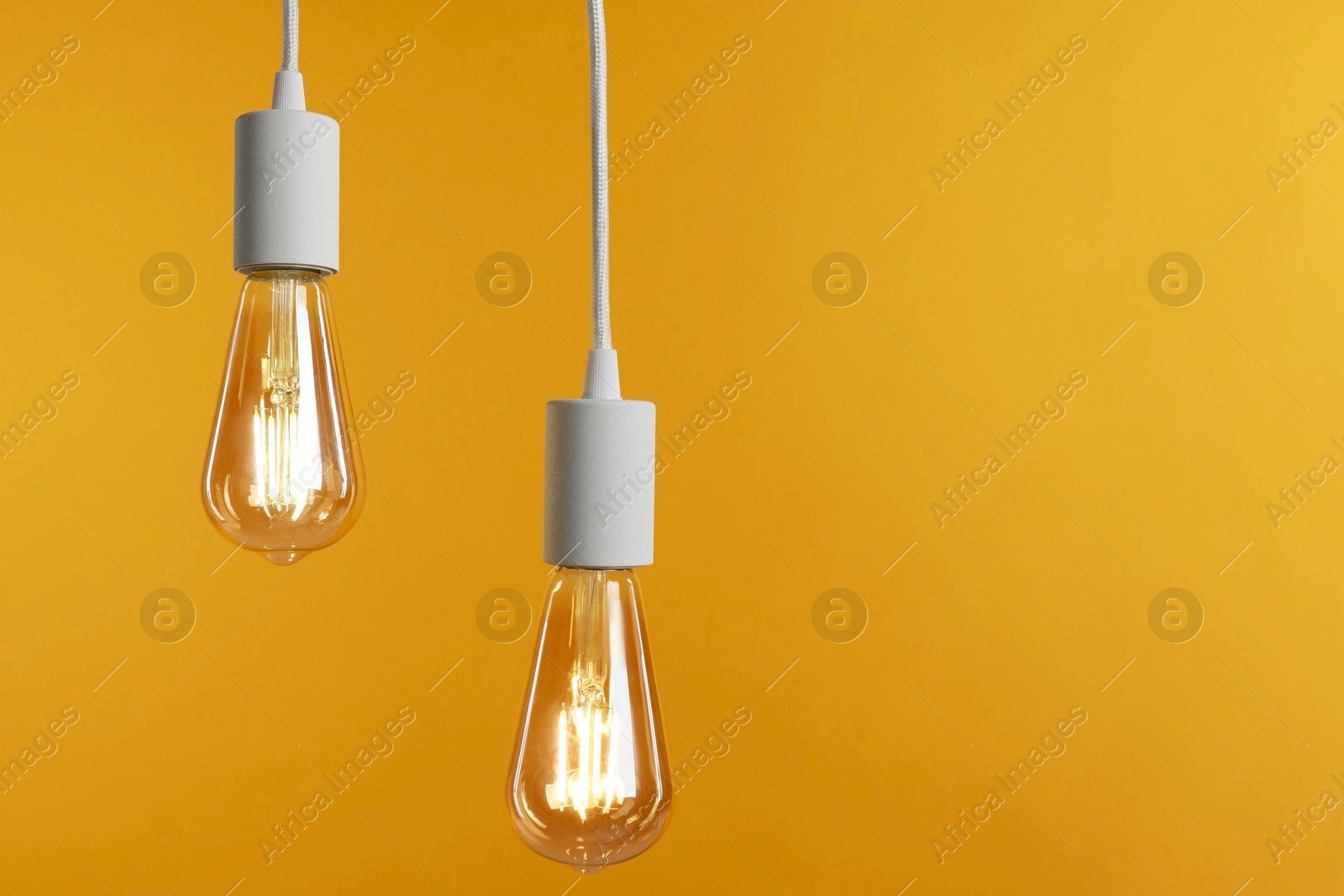 Photo of Light bulbs hanging on cords against orange background, space for text