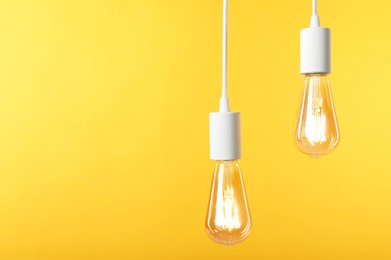 Photo of Light bulbs hanging on cords against orange background, space for text