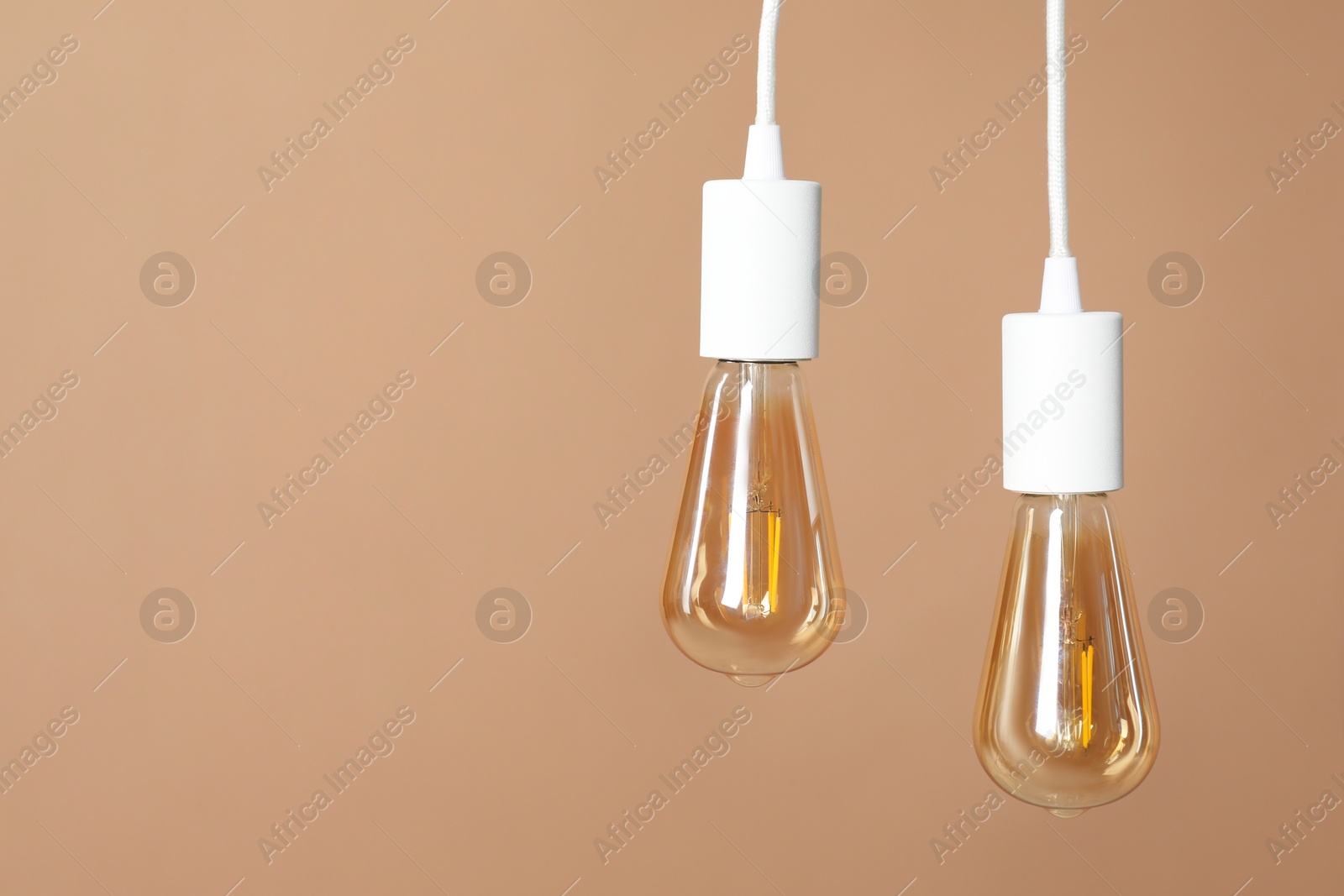 Photo of Light bulbs hanging on cords against beige background, space for text