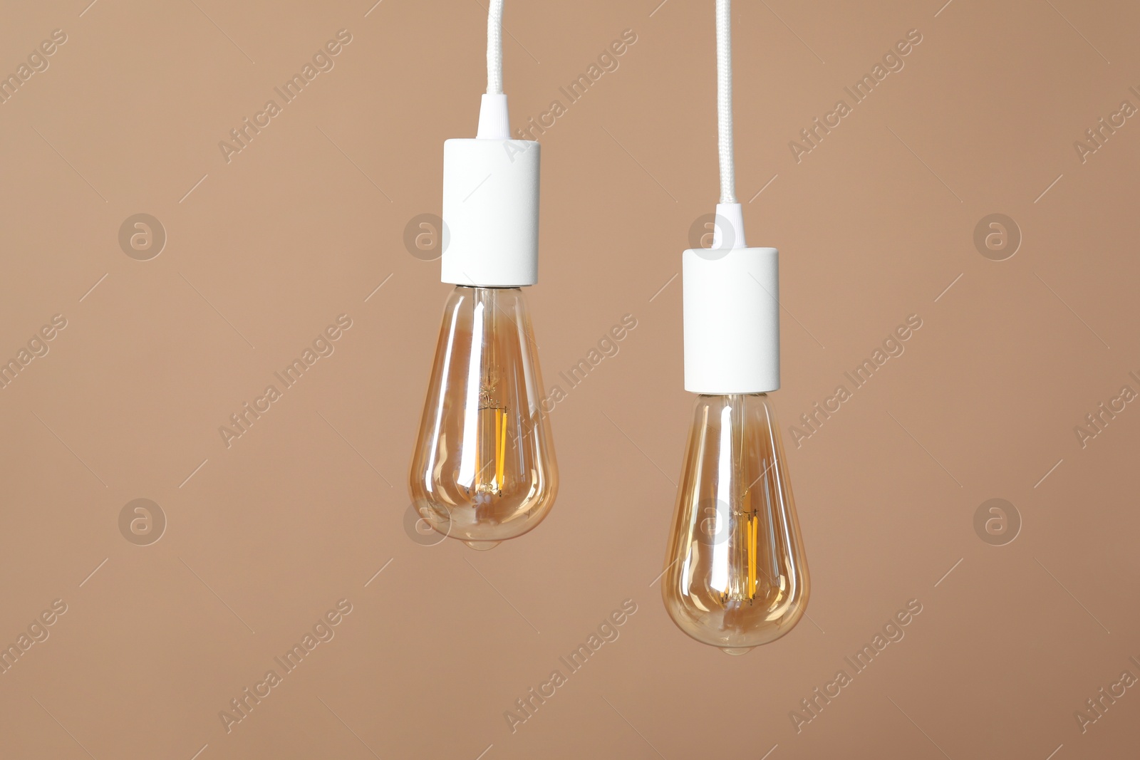 Photo of Light bulbs hanging on cords against beige background