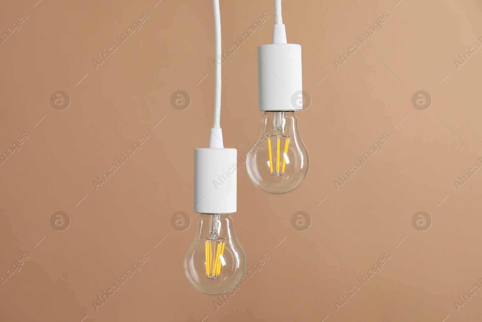 Photo of Light bulbs hanging on cords against beige background