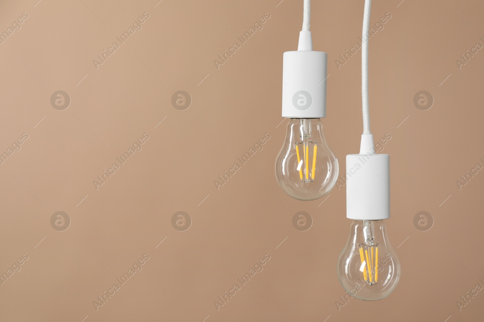 Photo of Light bulbs hanging on cords against beige background, space for text