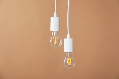 Photo of Light bulbs hanging on cords against beige background, space for text