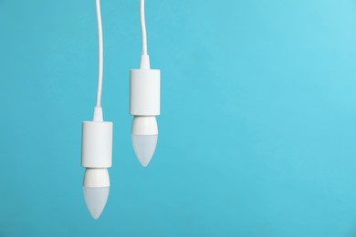 Photo of Light bulbs hanging on cords against blue background, space for text