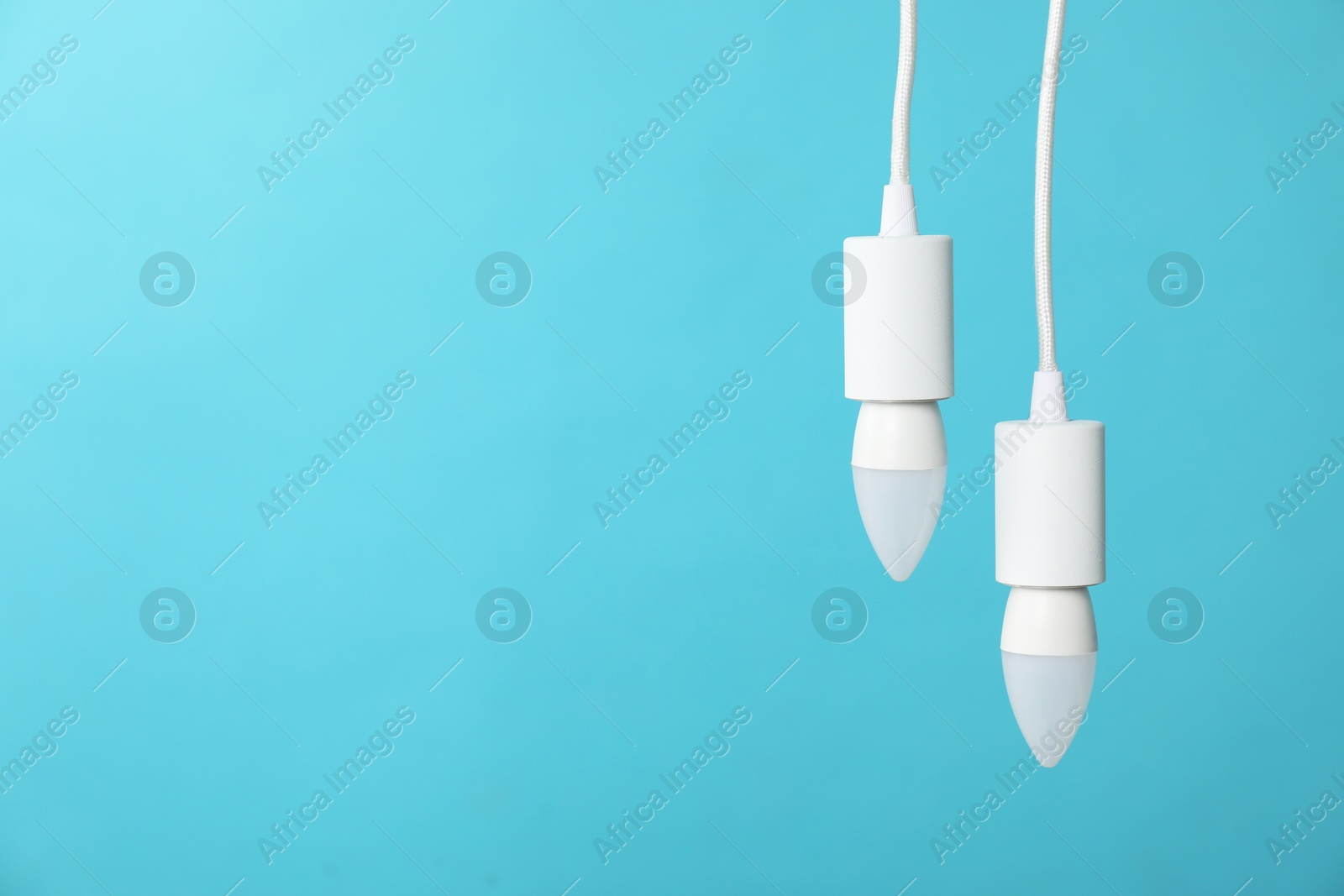 Photo of Light bulbs hanging on cords against blue background, space for text