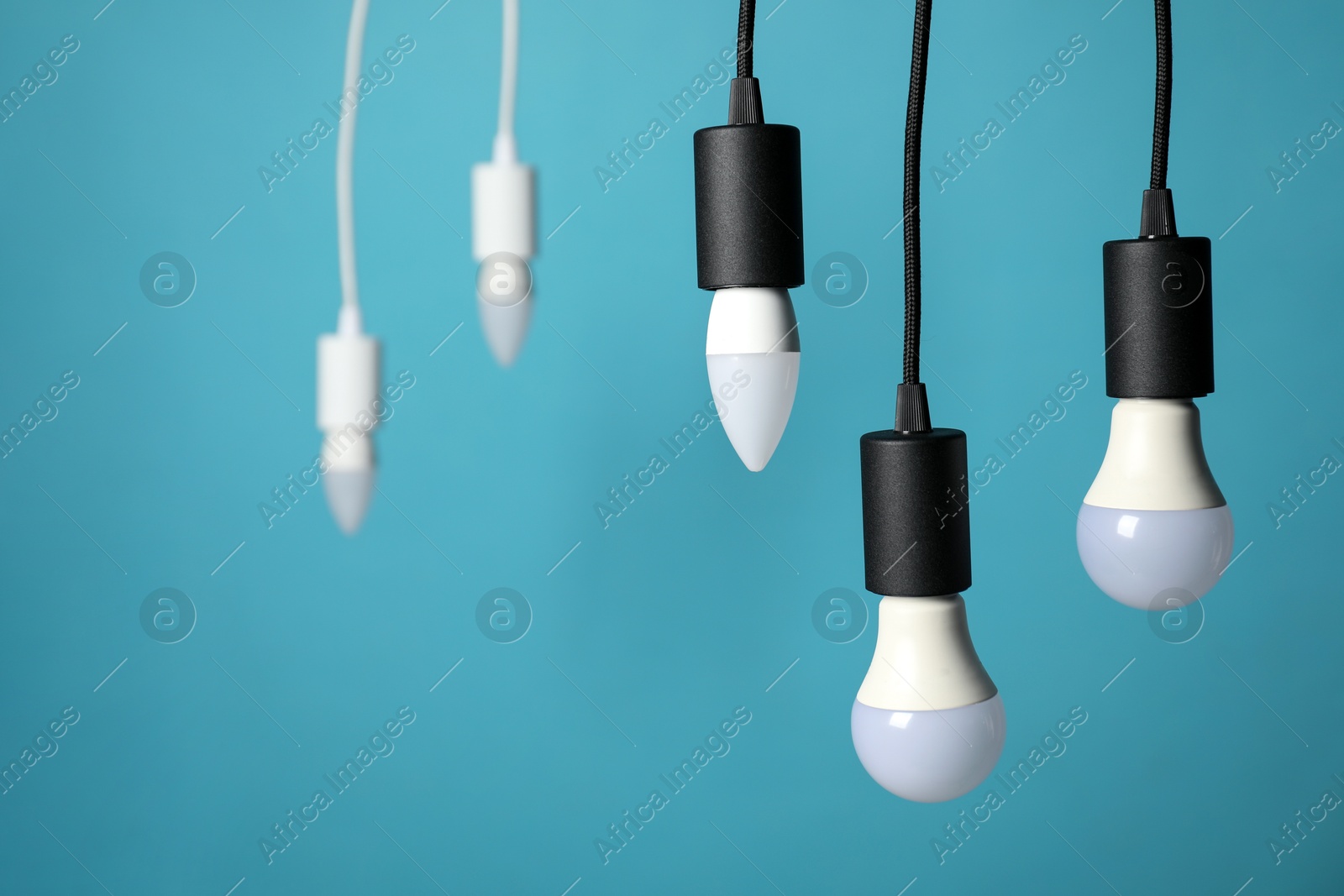 Photo of Light bulbs hanging on cords against blue background, selective focus