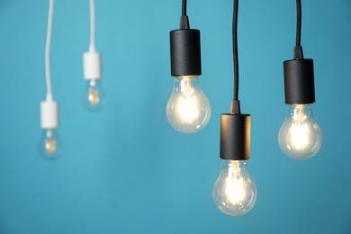 Photo of Light bulbs hanging on cords against blue background, selective focus