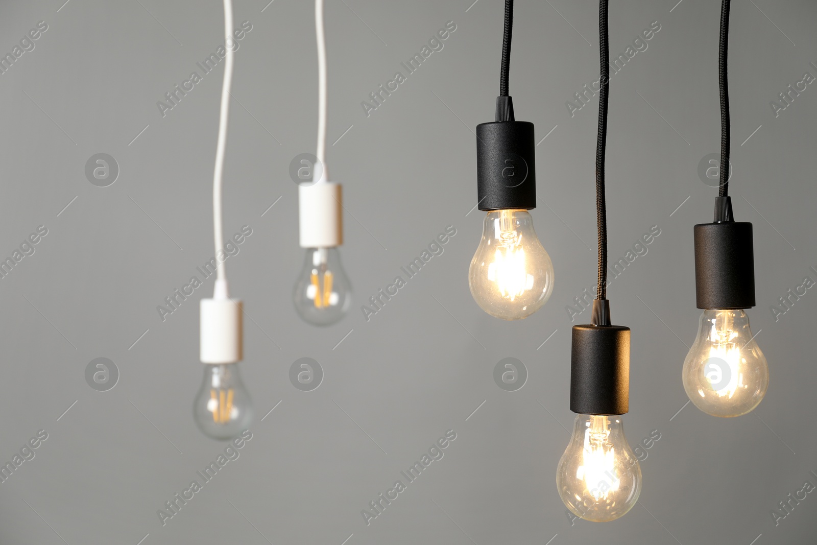 Photo of Light bulbs hanging on cords against grey background, selective focus