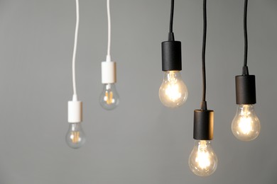 Photo of Light bulbs hanging on cords against grey background, selective focus