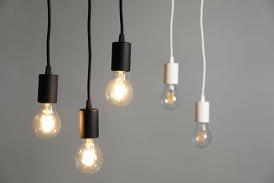 Photo of Light bulbs hanging on cords against grey background, selective focus