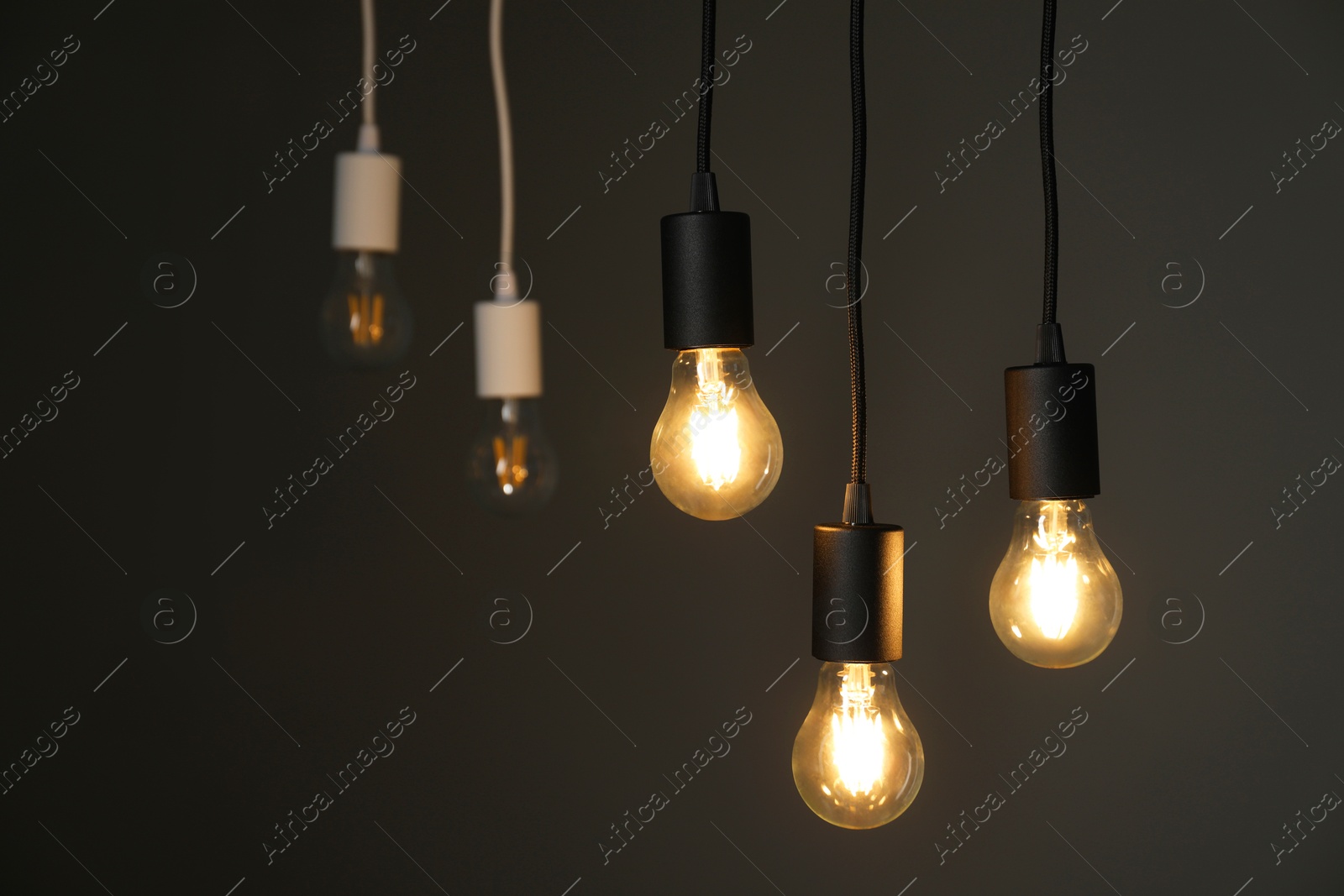 Photo of Light bulbs hanging on cords against grey background, selective focus