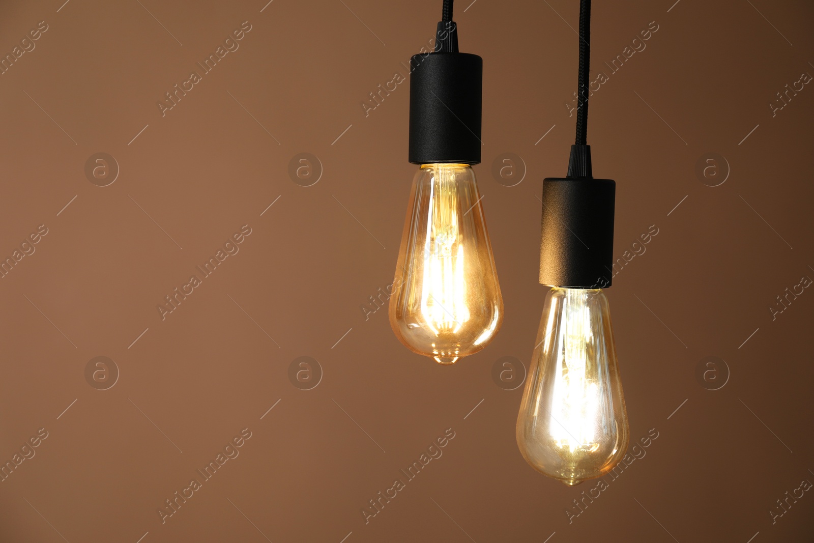 Photo of Light bulbs hanging on cords against brown background, space for text