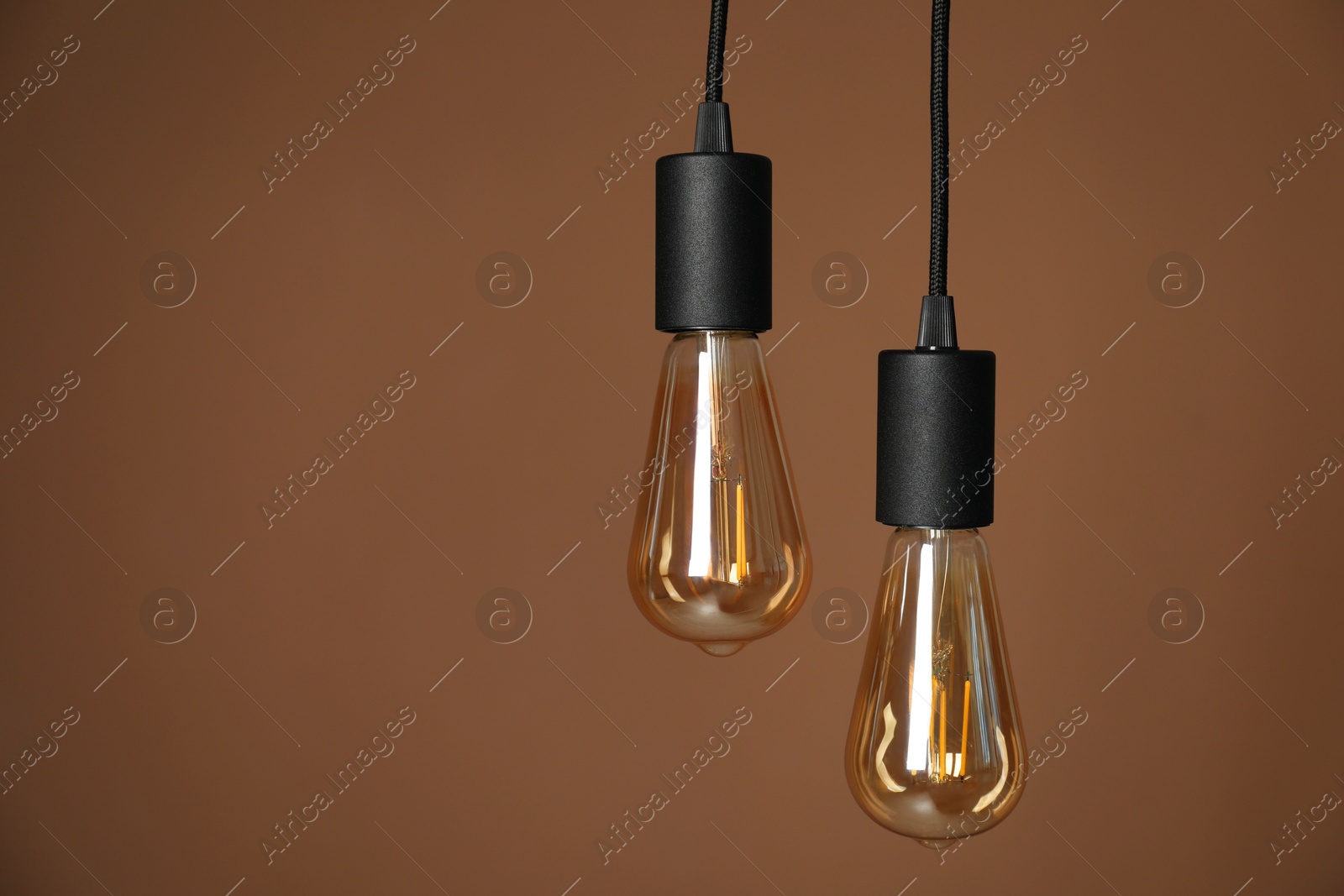 Photo of Light bulbs hanging on cords against brown background, space for text