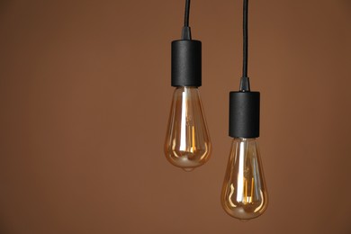 Photo of Light bulbs hanging on cords against brown background, space for text