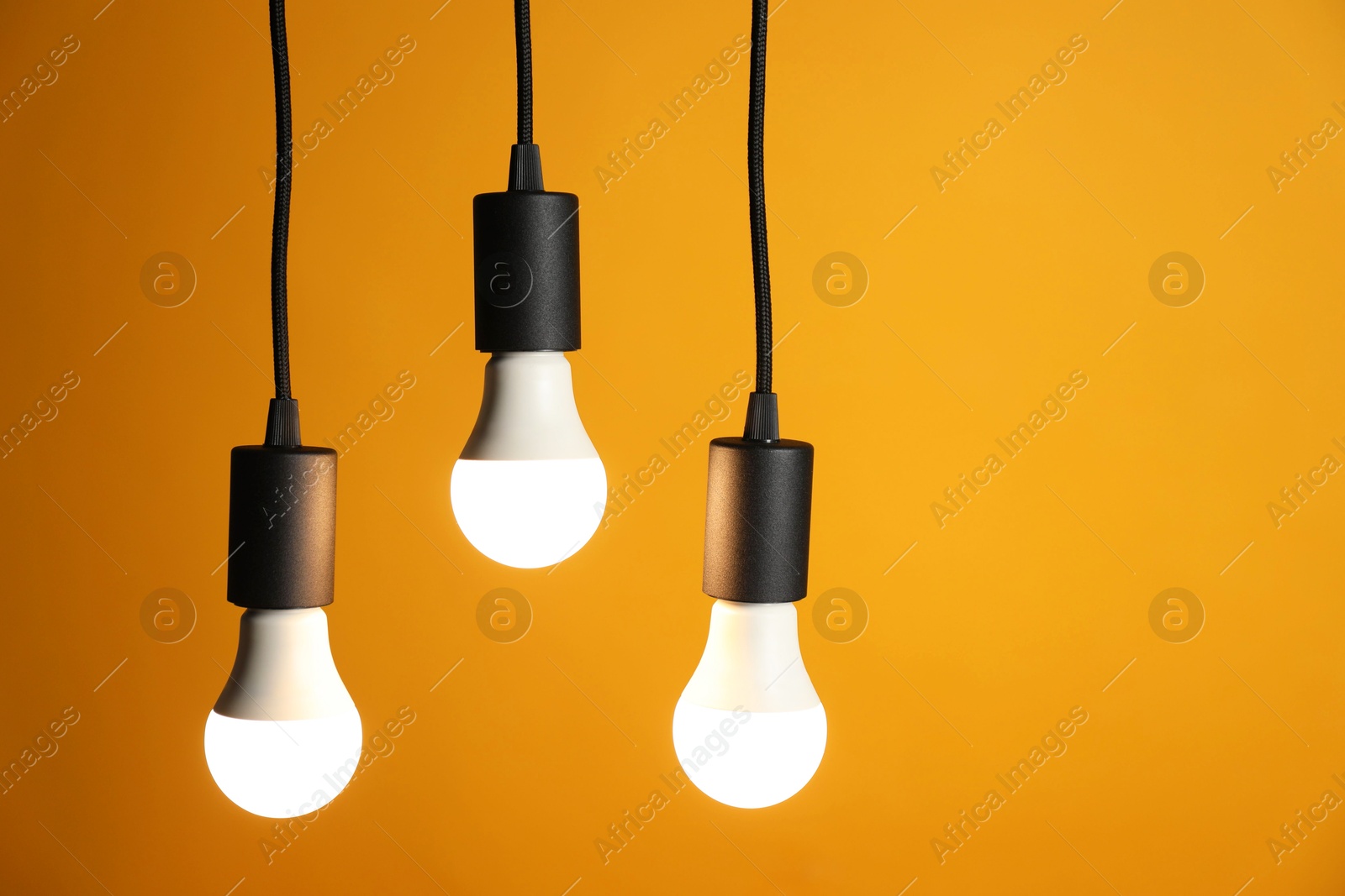 Photo of Light bulbs hanging on cords against orange background, space for text