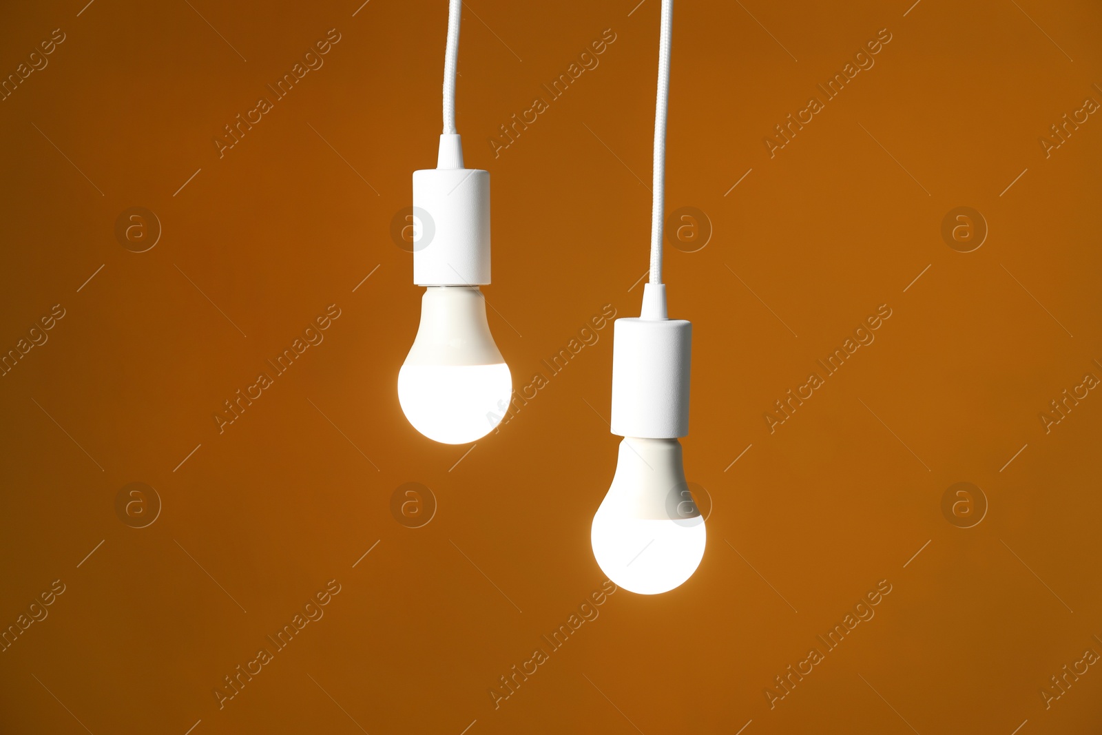 Photo of Light bulbs hanging on cords against orange background