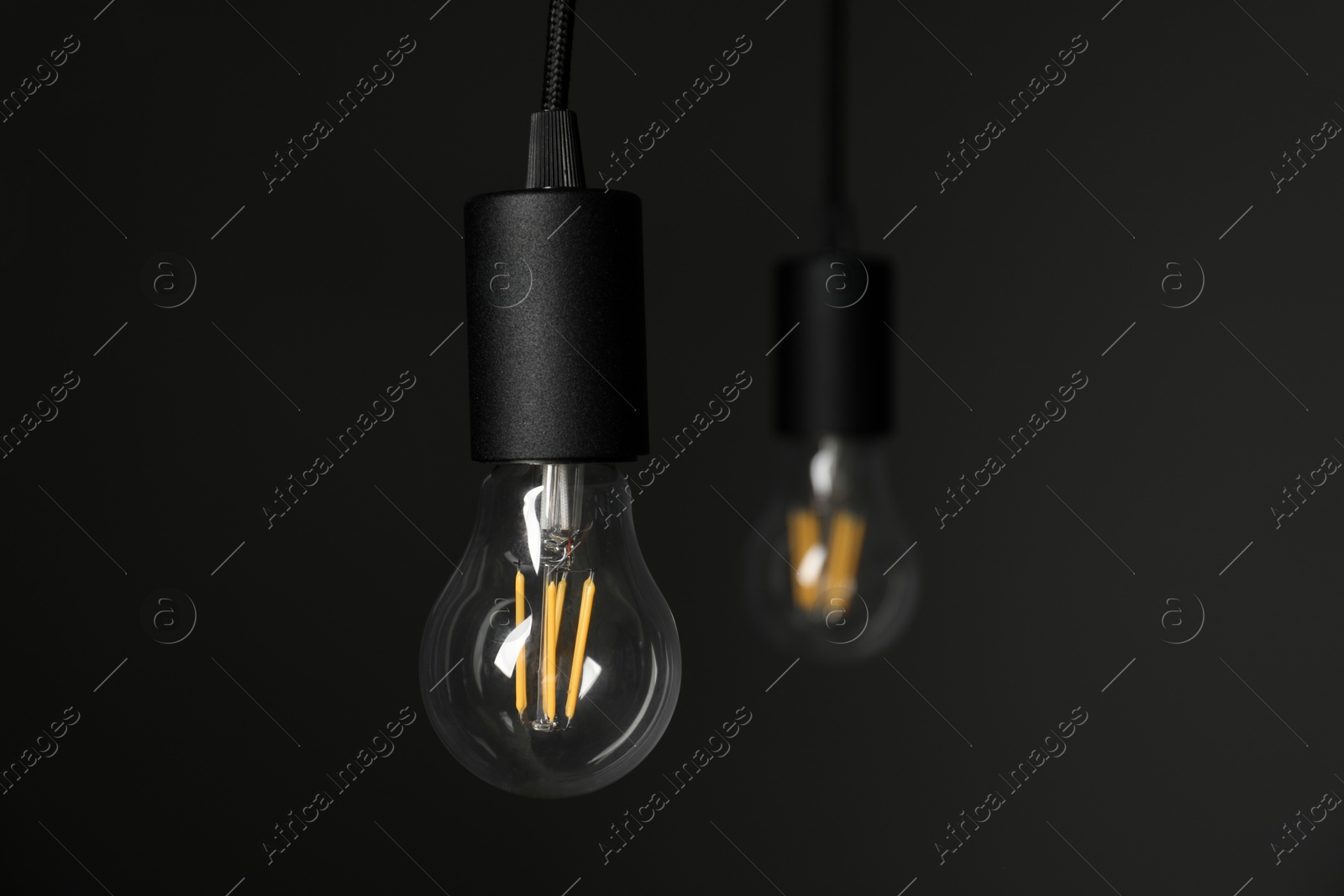 Photo of Light bulbs hanging on cords against grey background, selective focus. Space for text