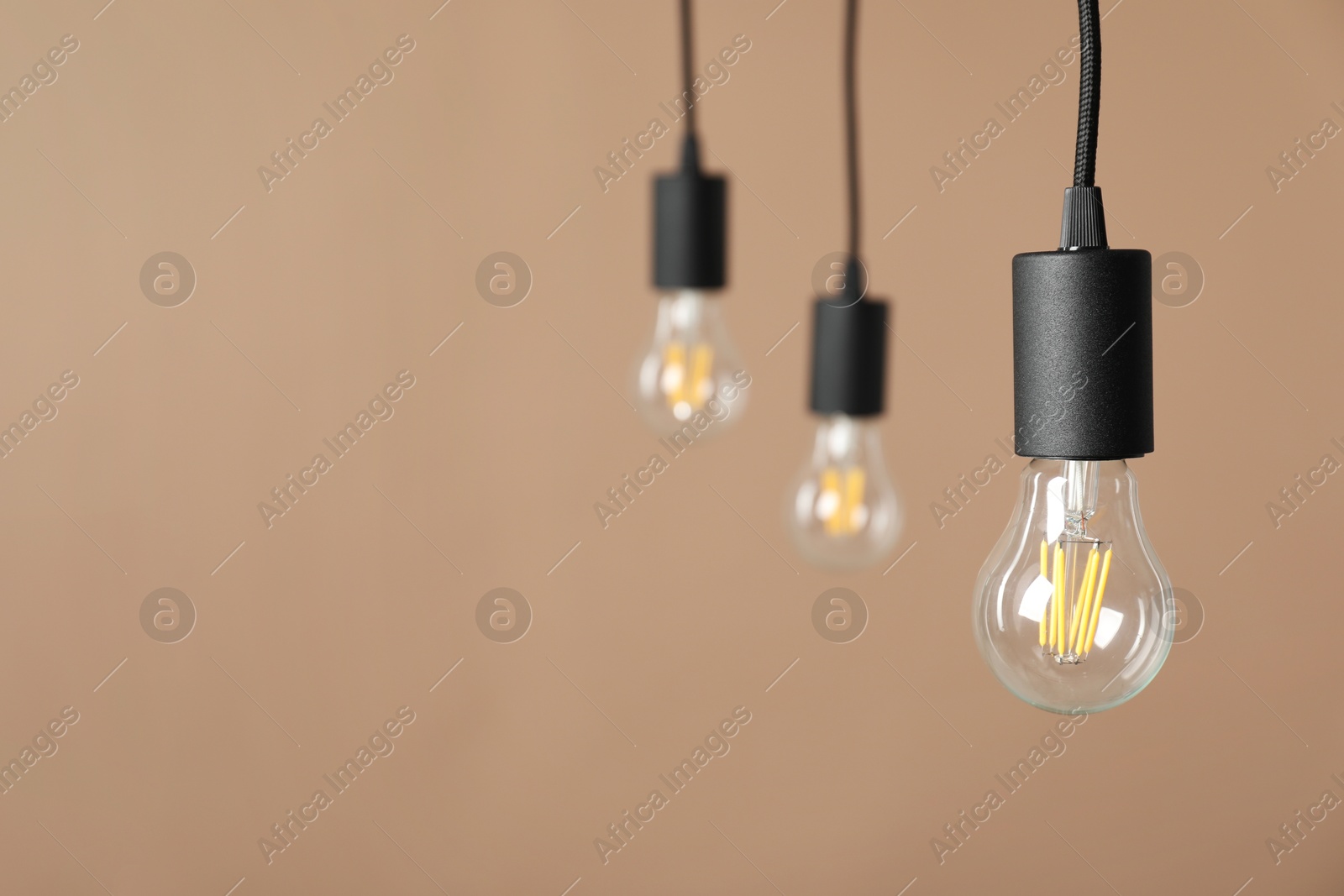 Photo of Light bulbs hanging on cords against beige background, selective focus. Space for text