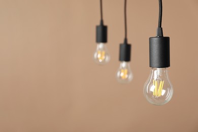 Photo of Light bulbs hanging on cords against beige background, selective focus. Space for text