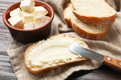 Photo of Fresh bread with butter and knife on wooden table, closeup