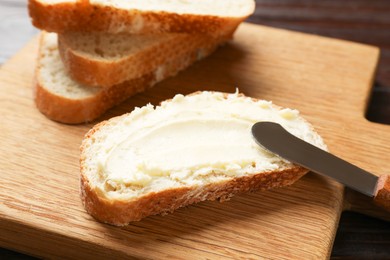 Photo of Fresh bread with butter and knife on wooden board, closeup