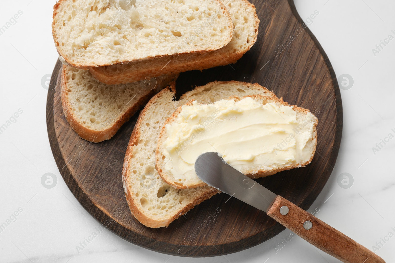 Fresh bread with butter and knife on white table, top view Photo of Fresh bread with butter and knife on white table, top view