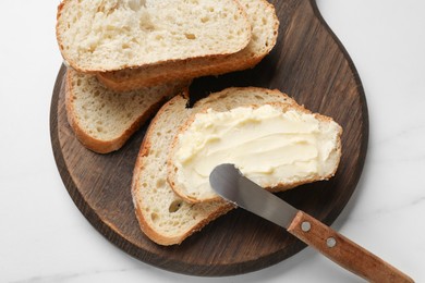 Photo of Fresh bread with butter and knife on white table, top view