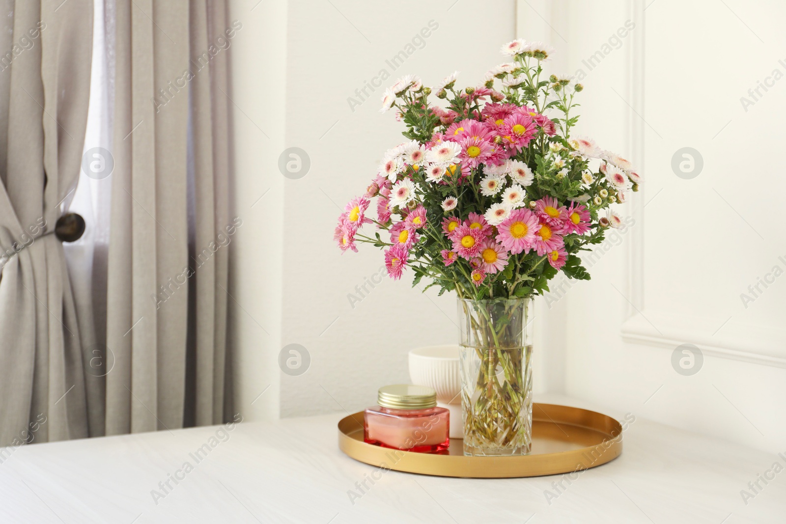 Photo of Beautiful flowers in vase and candles on white wooden table at home