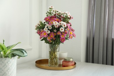 Photo of Beautiful flowers in vase and candles on white wooden table at home