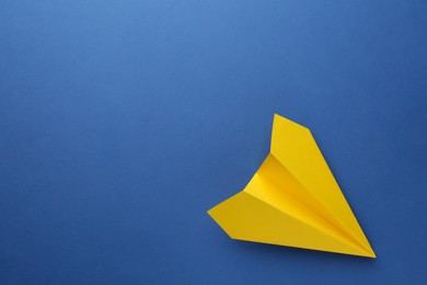 Photo of One handmade yellow paper plane on blue background, top view. Space for text