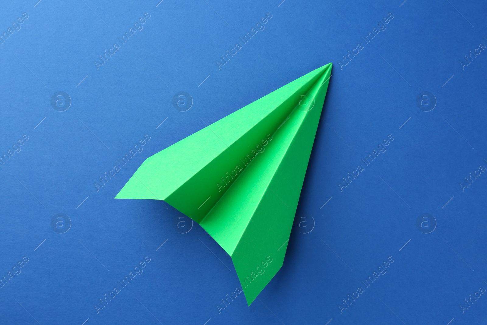 Photo of One handmade green paper plane on blue background, top view