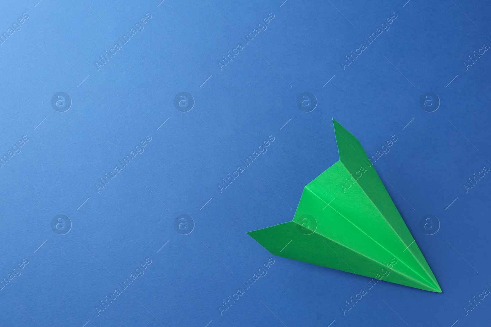 Photo of One handmade green paper plane on blue background, top view. Space for text