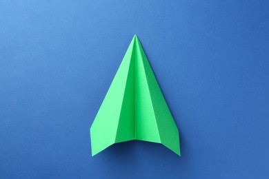 Photo of One handmade green paper plane on blue background, top view