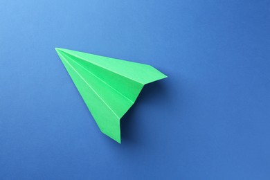 Photo of One handmade green paper plane on blue background, top view. Space for text